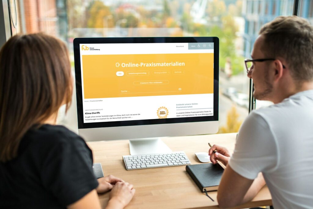zwei Personen vor einem Monitor, auf dem die Online-Praxismaterialien-Datenbank des Forum Umweltbildung zu sehen ist