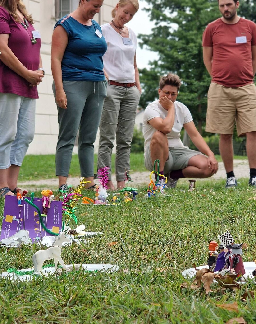 Menschen stehen im Kreis auf Wiese und sehen selbstgebastelte Prototypen an.
